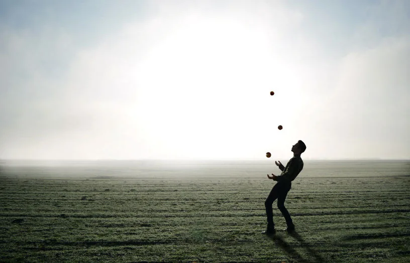 A man juggling in an open field under a bright sky
